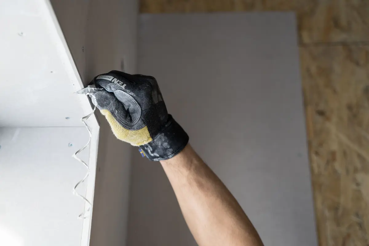 A fitter fixing plasterboard to a new partition