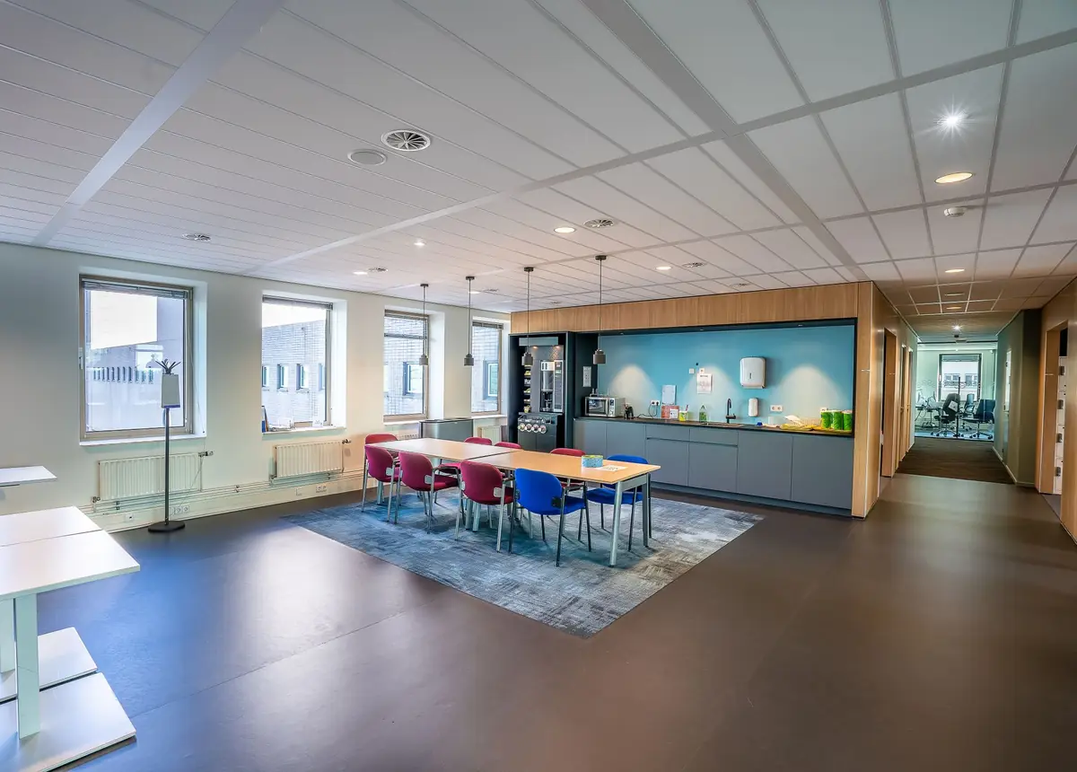 Bright open-plan office with a long team table and a kitchen wall